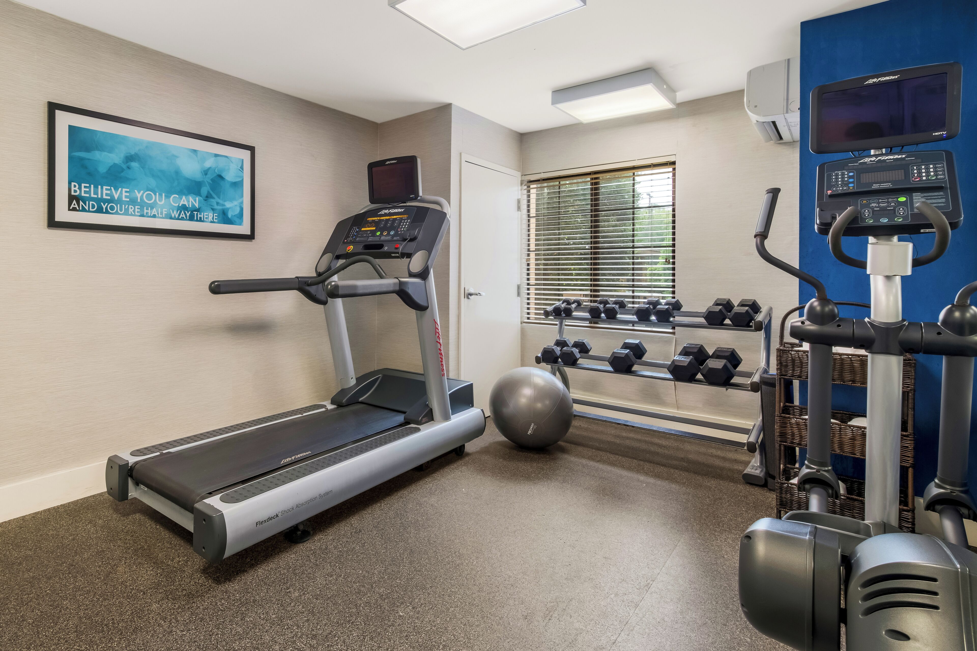 A gym with a treadmill, dumbbells, a stationary bike, and a motivational poster.