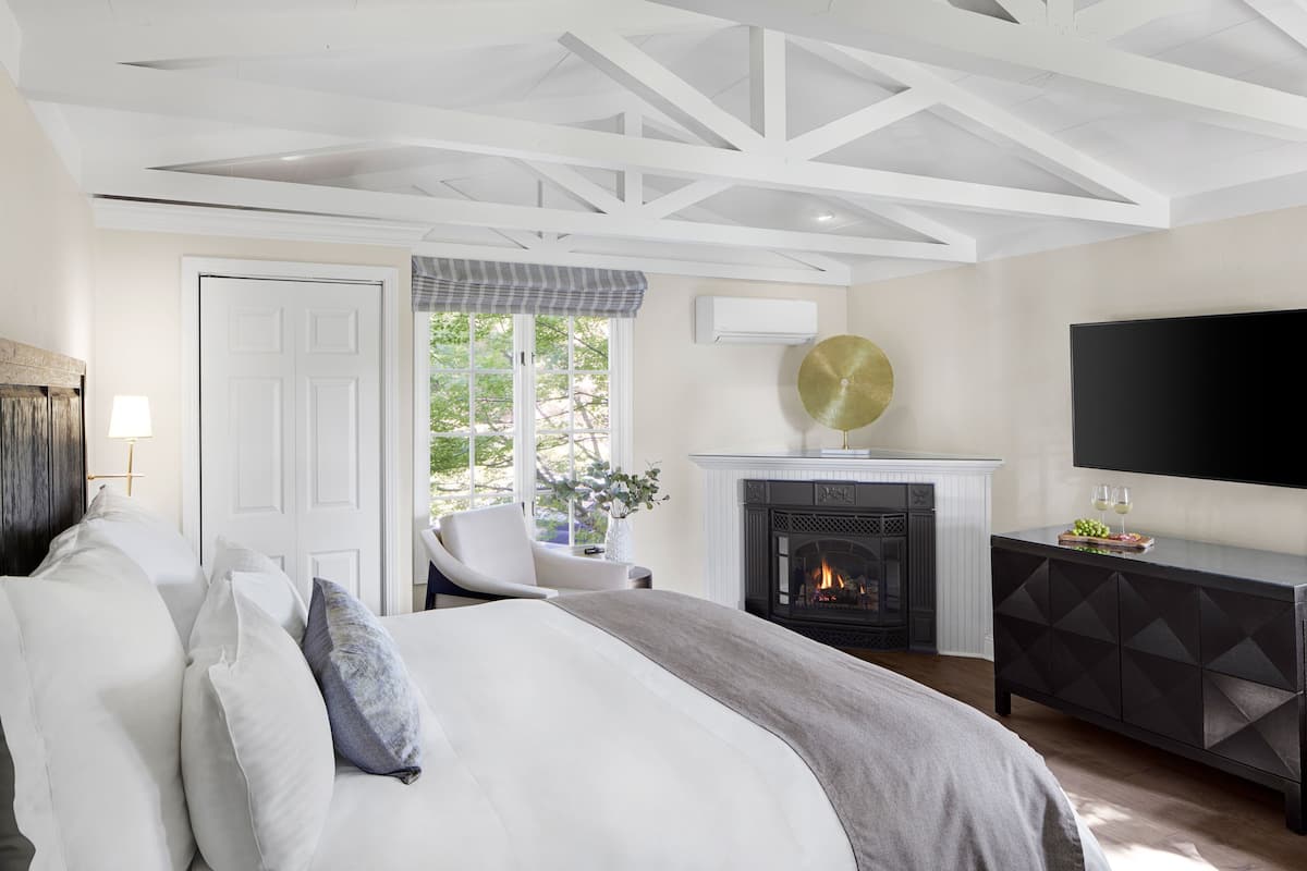 A bedroom with a bed, a chair, a fireplace, and a TV.
