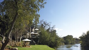 A riverside property with a well-maintained lawn, outdoor seating, and a building with a balcony overlooking the water.