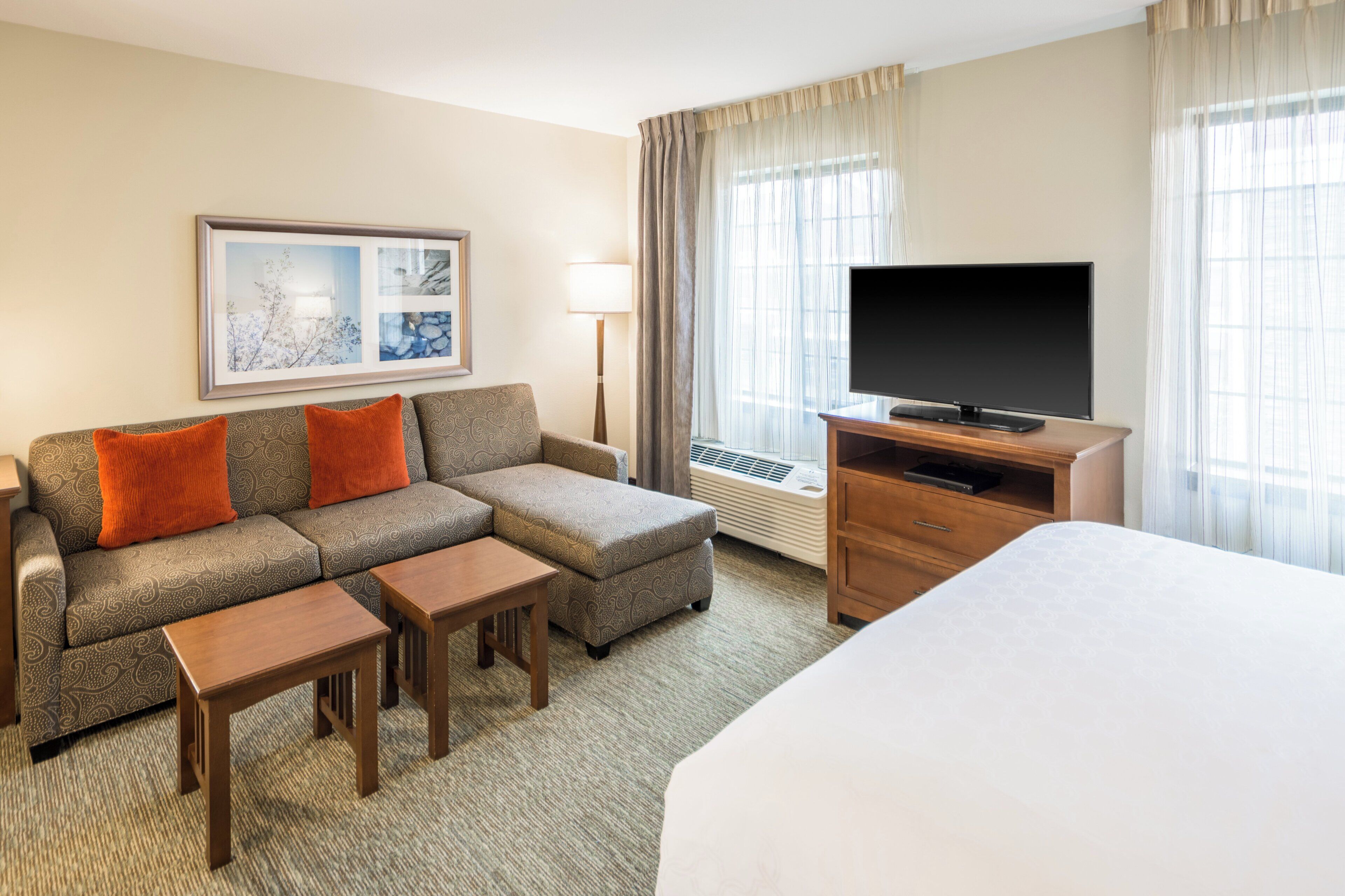 Ein Hotelzimmer mit einer Couch, einem Hocker, einem Couchtisch, einem Fernseher und einem Bett.