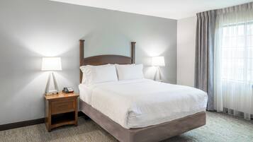 Habitación de hotel con cama, dos lámparas de noche, mesita de noche con teléfono y ventana con cortinas.