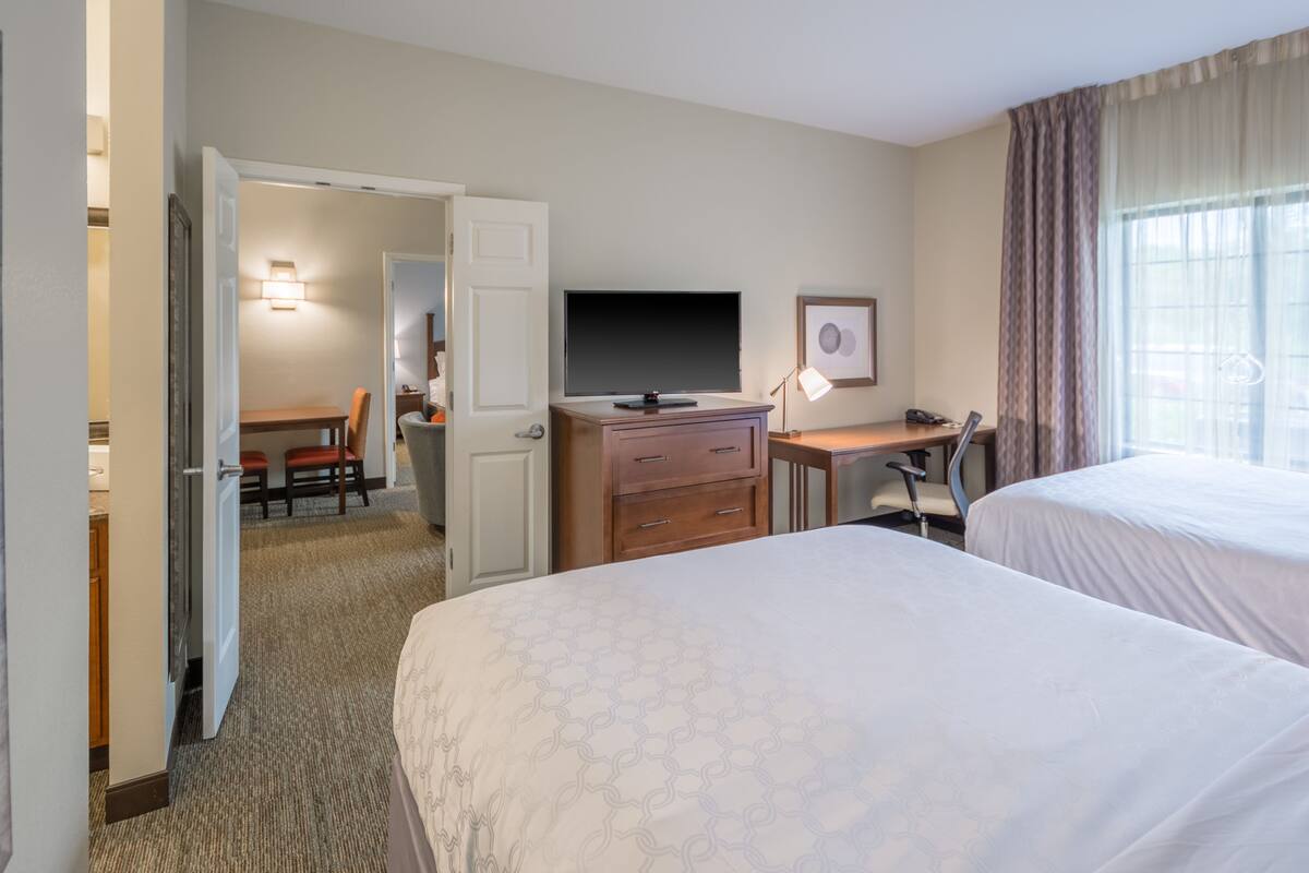 Une chambre d’hôtel avec deux lits, un bureau avec un ordinateur, une télévision et un coin repas avec des chaises.