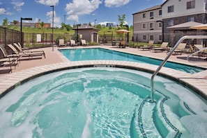 A swimming pool with a hot tub, surrounded by lounge chairs and a fence.
