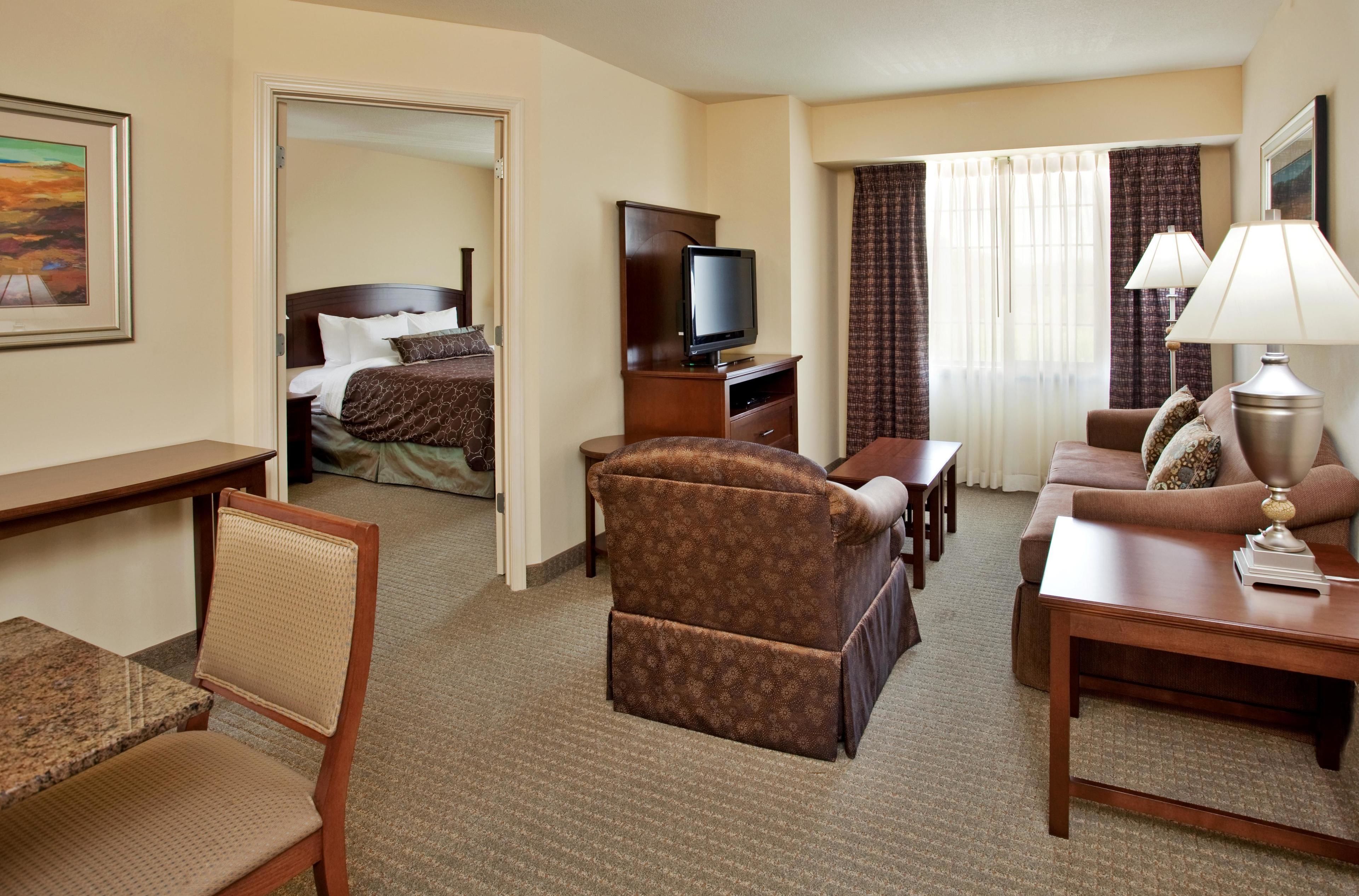 A hotel room with a bed, a television, a desk, a chair, a sofa, and a lamp.