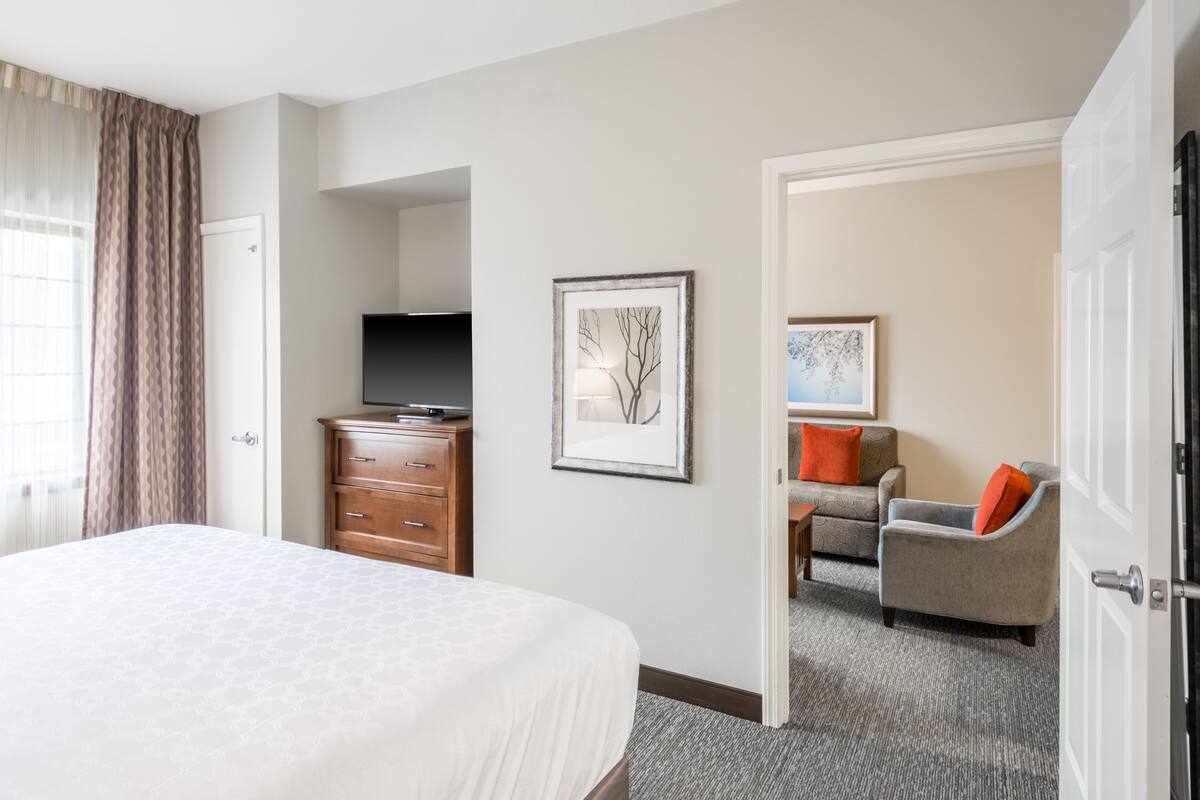 Une chambre d’hôtel avec un grand lit, une commode, une télévision et un coin salon comprenant une chaise et un canapé.