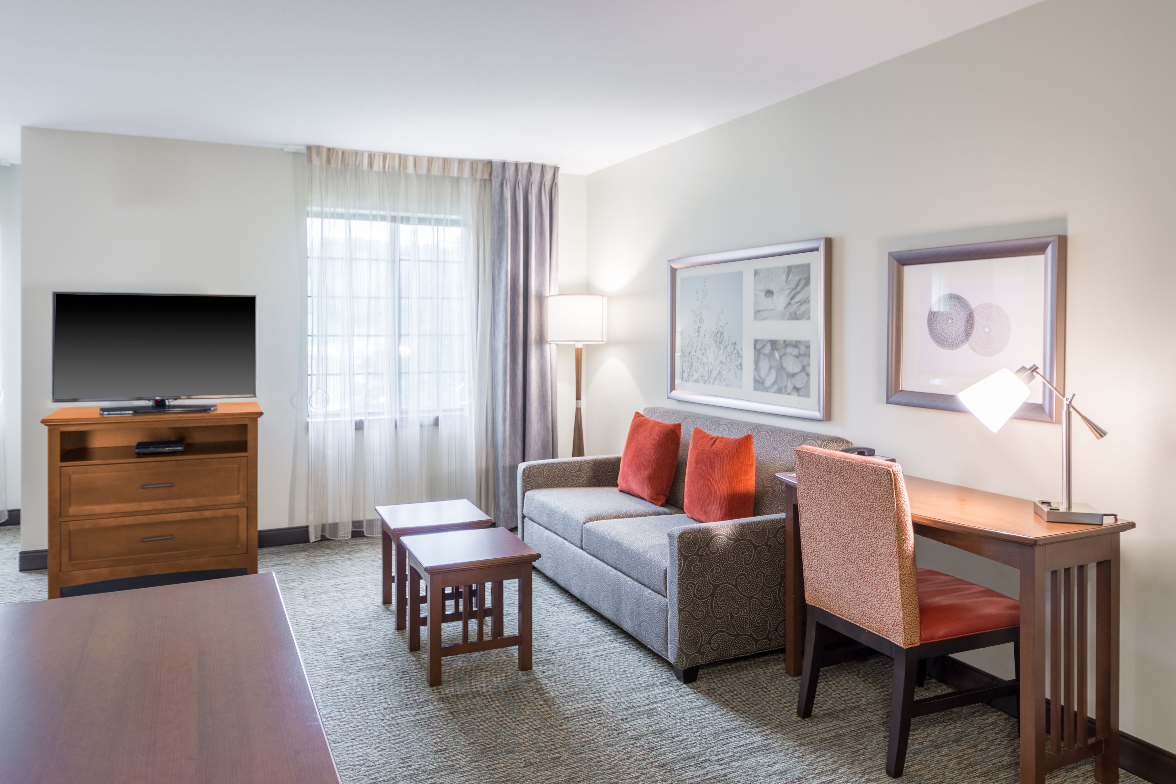 A hotel room with a flat-screen TV, a sofa, a dining table, and a chair.