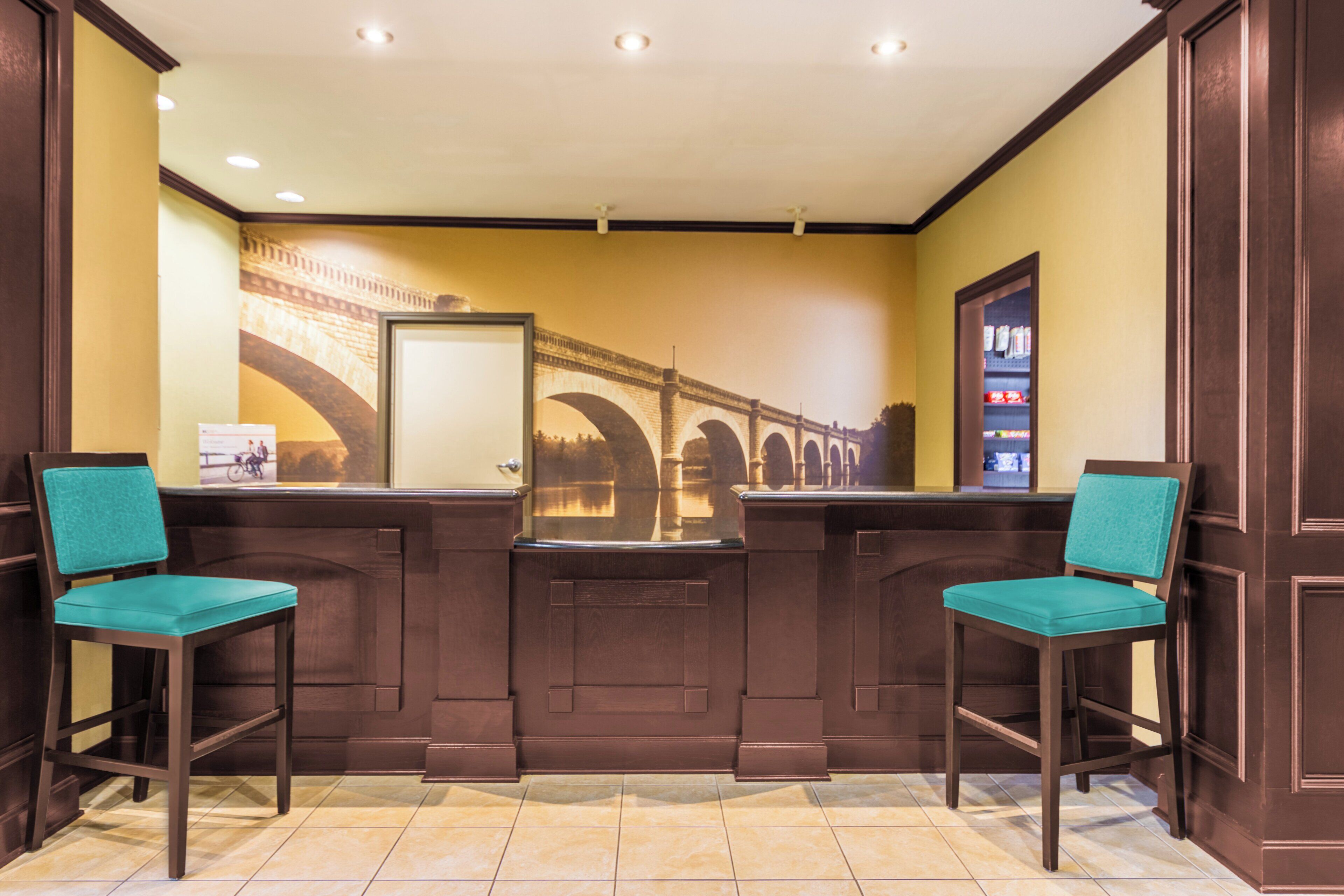 A reception area with a counter, two chairs, a wall-mounted mirror, and a shelf with items.