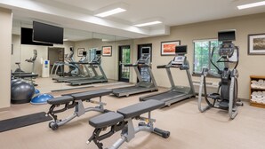 Une salle de sport équipée de tapis de course, de vélos elliptiques et de bancs d’exercices.