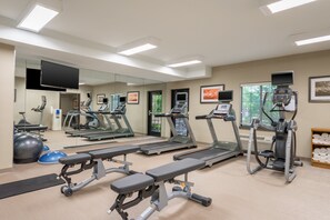 Ein Fitnessstudio mit Laufbändern, Crosstrainern und Trainingsbänken.