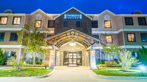 L’entrée d’un hôtel Staybridge Suites, avec une façade en pierre, une enseigne au-dessus de l’entrée et un chemin bien éclairé menant à la porte.