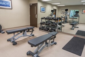 Ein Fitnessstudio mit Gewichtbänken, Kurzhanteln, Laufbändern und Trainingsgeräten.