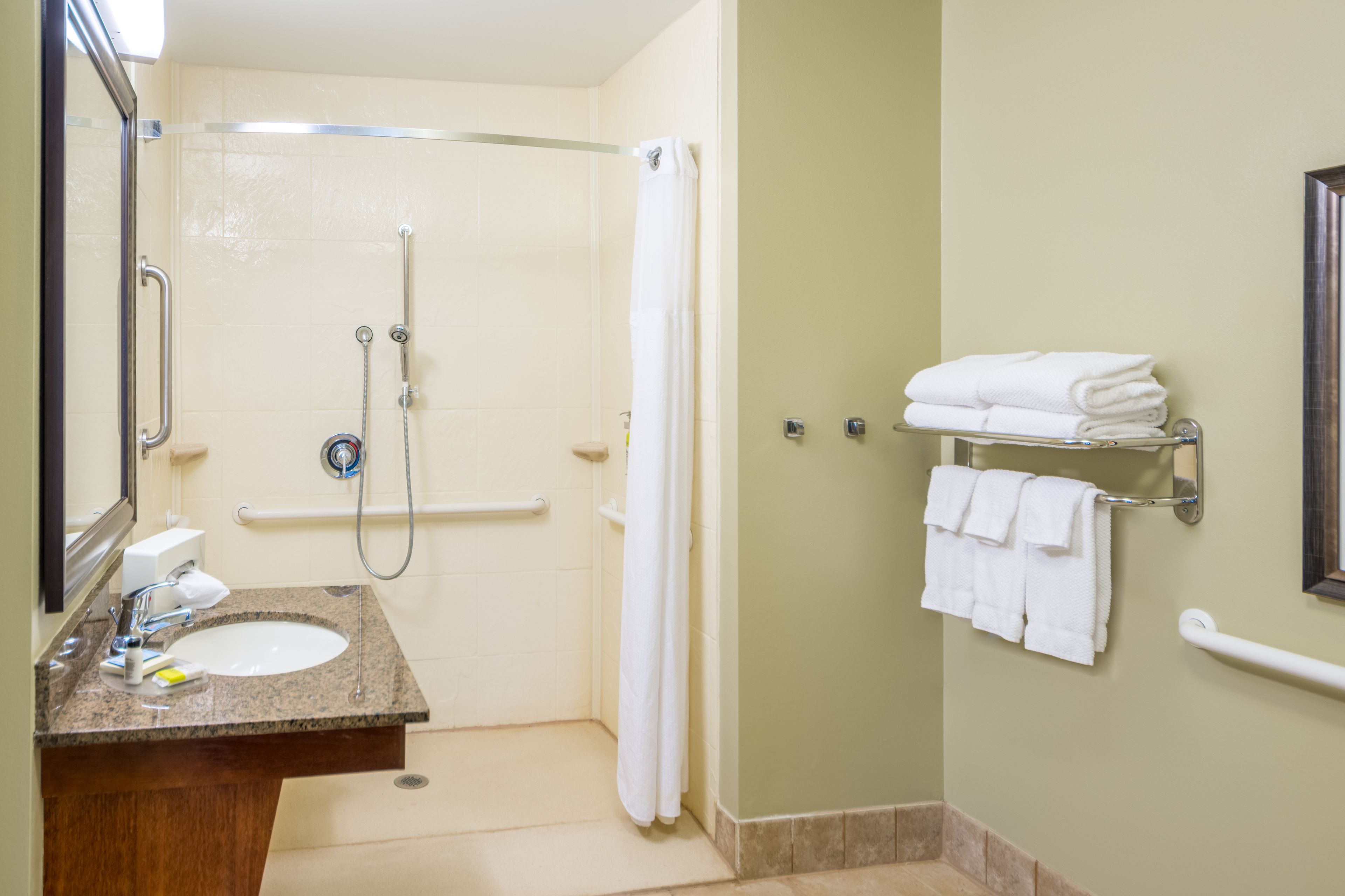 A bathroom with a sink, mirror, shower, and towel rack.