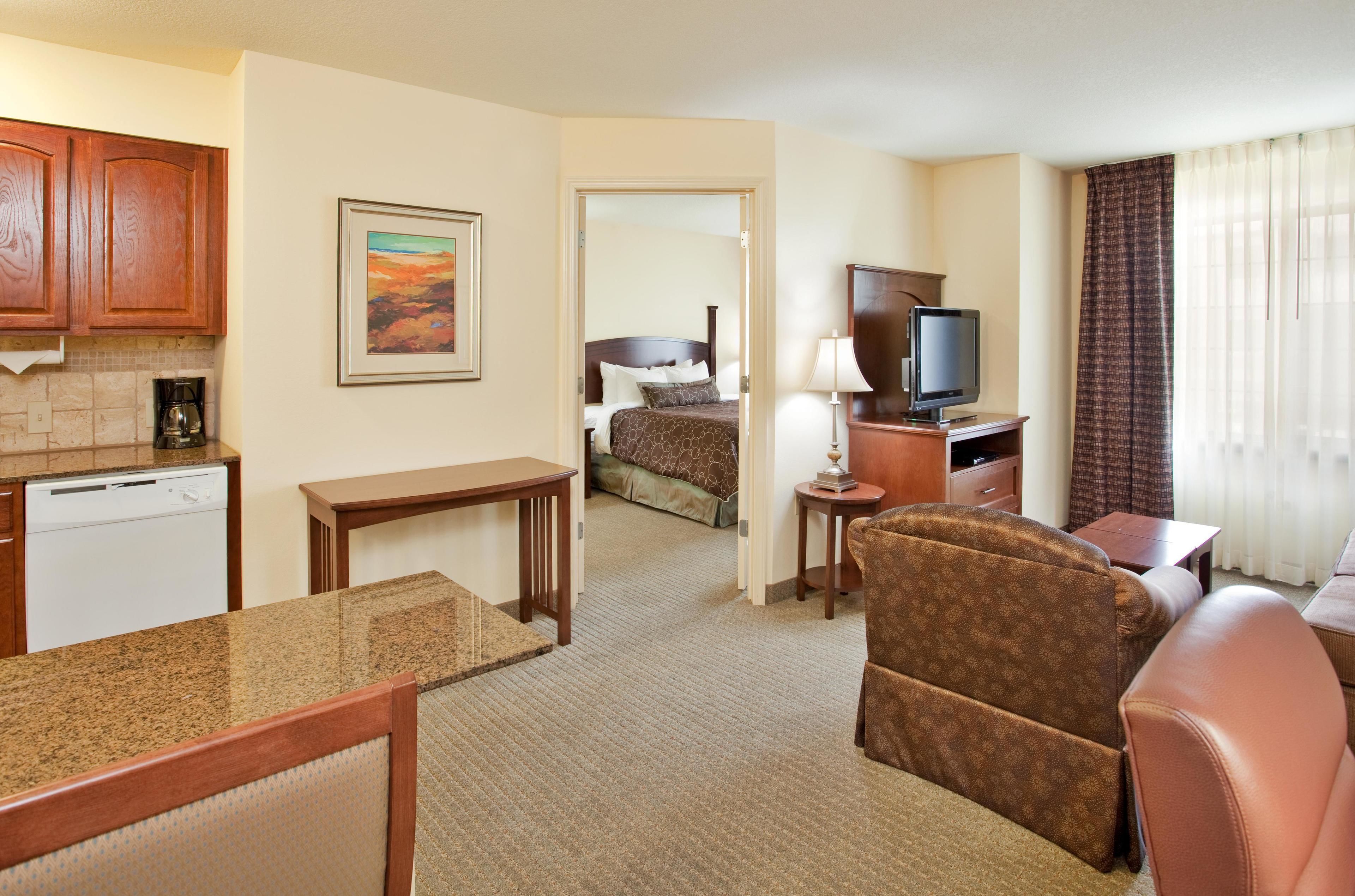 A hotel room with a kitchenette, a bed, a TV, a desk, and a chair.