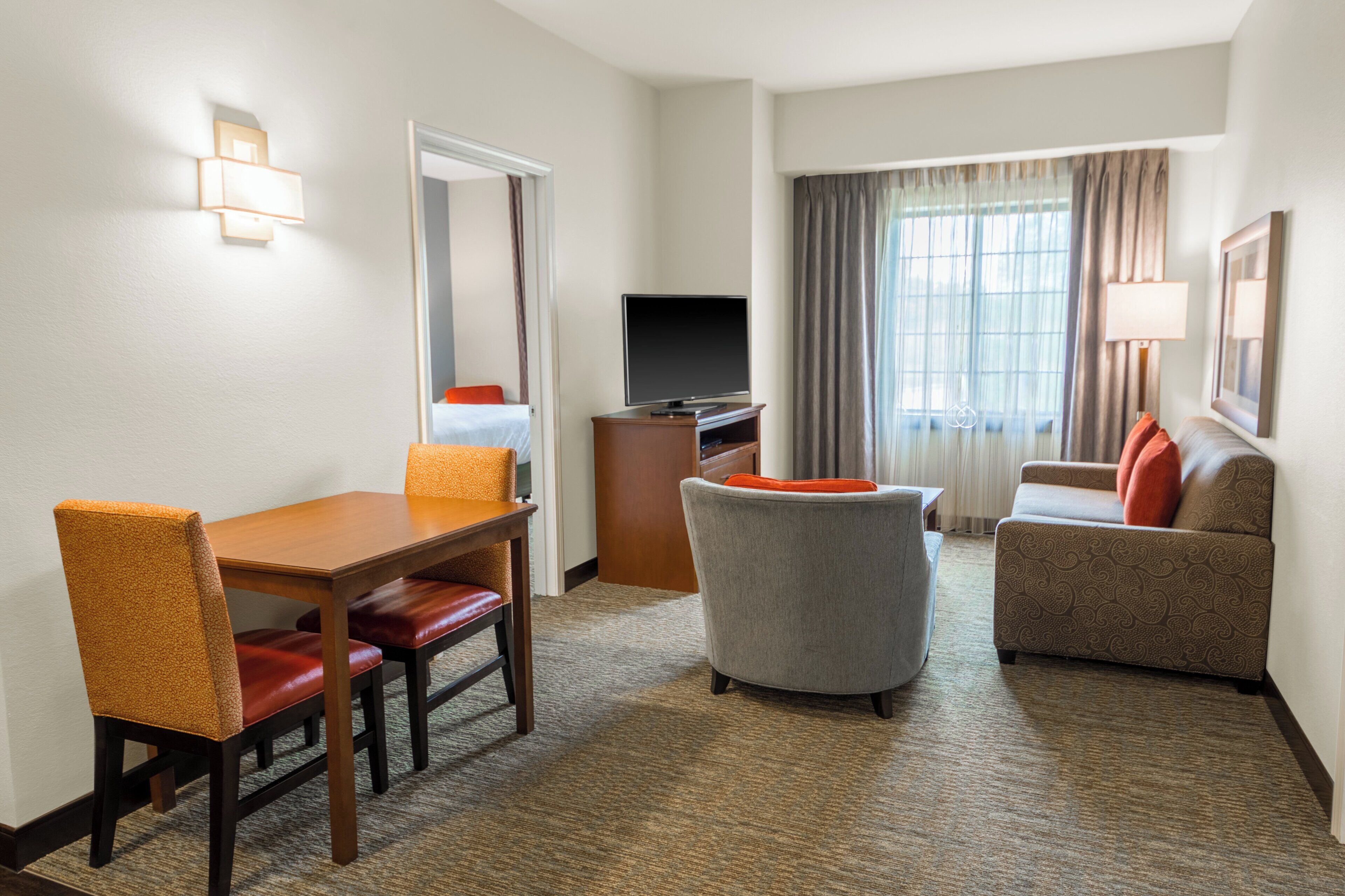 Una habitación de hotel con una mesa de comedor, dos sillas, un sofá, un televisor y una ventana con cortinas.