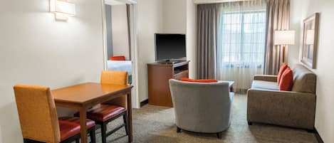 Una habitación de hotel con una mesa de comedor, dos sillas, un sofá, un televisor y una ventana con cortinas.