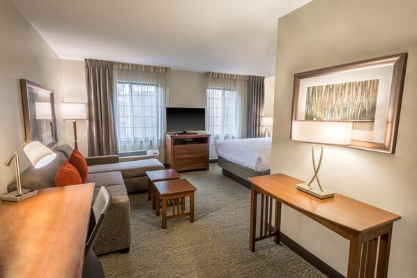 A hotel room with a sofa, a bed, a desk, a TV, and a painting on the wall.