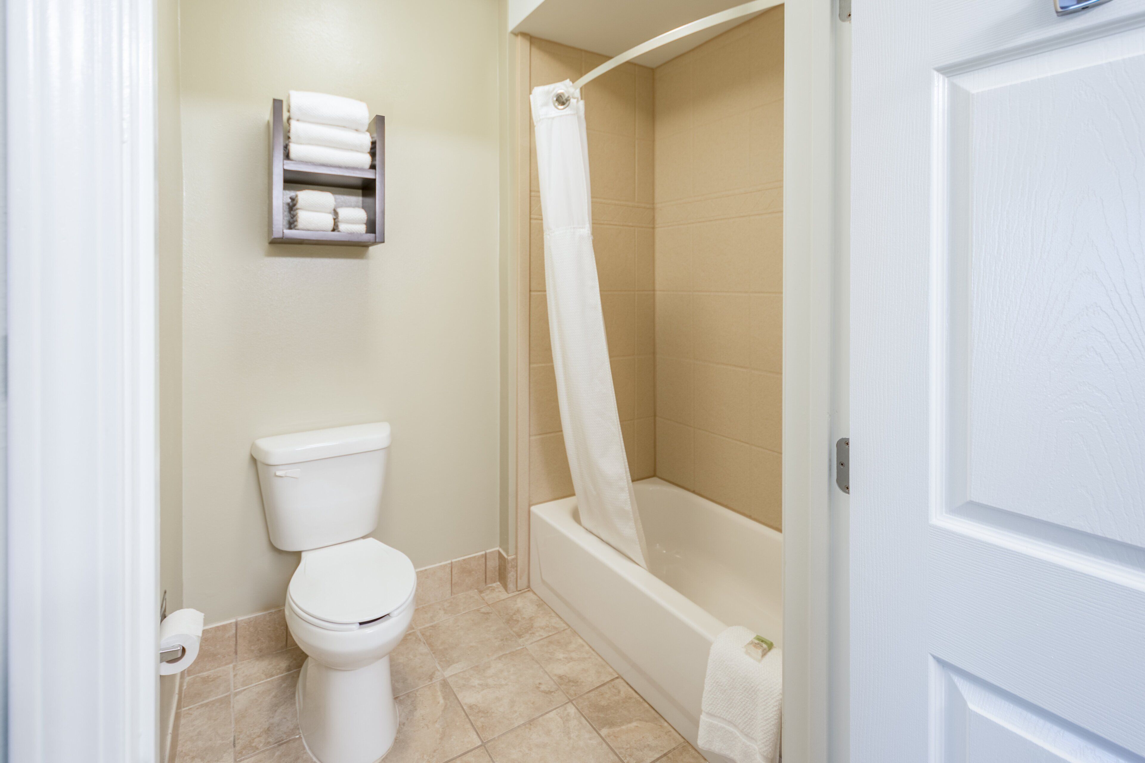A bathroom with a toilet, a shower with a curtain, and a towel rack with towels.