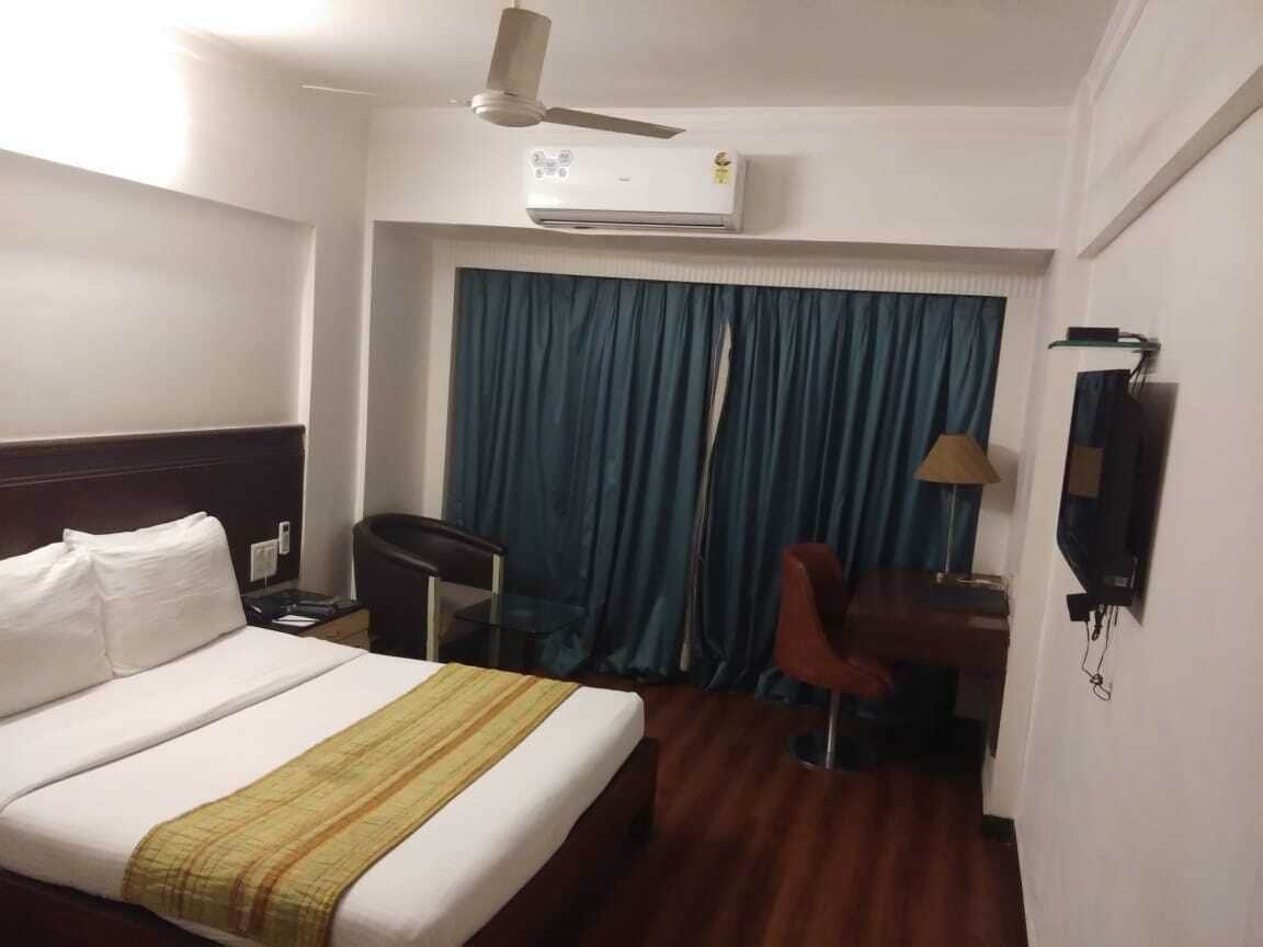 A hotel room with a bed, a desk, a chair, a desk lamp, a TV, and a ceiling fan.