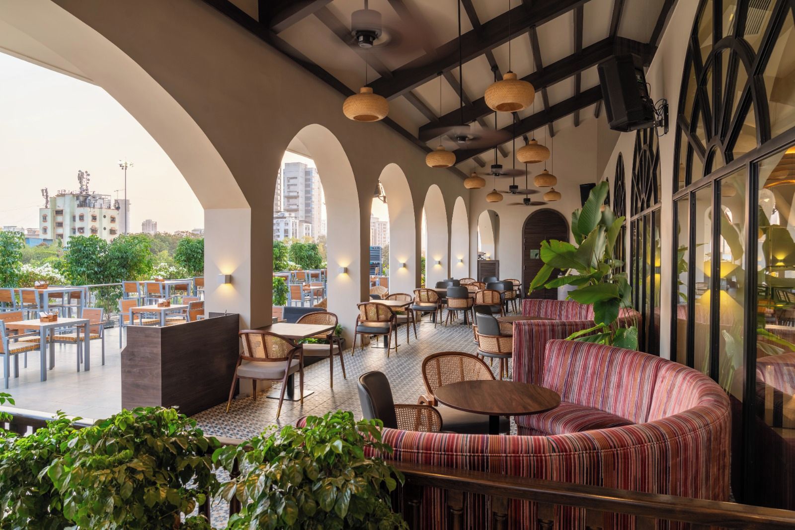 An outdoor seating area with tables and chairs, a striped sofa, and potted plants.