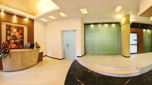 A hotel lobby with a reception desk, a staircase, and a green textured wall. - Yogi Metropolitan (Navi Mumbai)