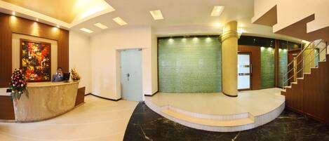 A hotel lobby with a reception desk, a staircase, and a green textured wall.