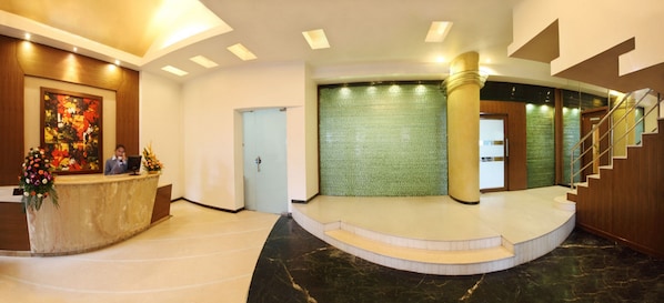 Un hall d’hôtel avec un comptoir d’accueil, un escalier et un mur texturé de couleur verte.