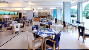 A spacious restaurant with multiple dining tables and chairs, a bar area, and large windows offering a view of the outdoors. - Yogi Metropolitan (Navi Mumbai)