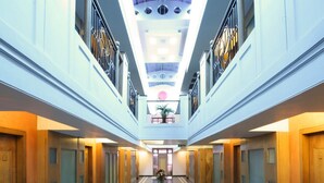 A hotel corridor with a marble floor, wooden doors, and a central skylight. - Yogi Metropolitan (Navi Mumbai)