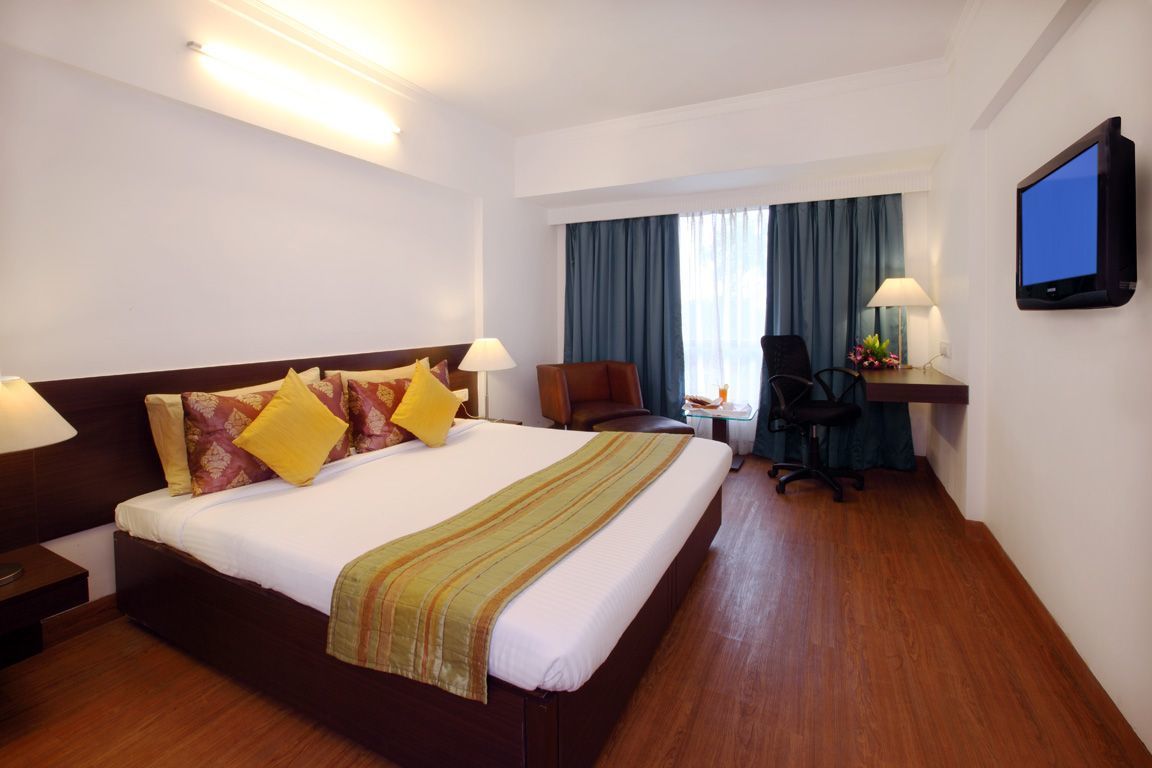 Una habitación de hotel con una cama grande, un escritorio con silla, un televisor y una ventana con cortinas.