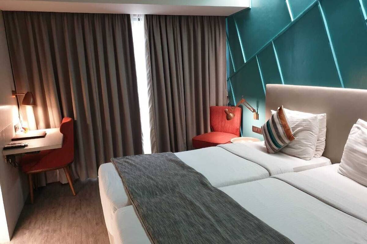 Una habitación de hotel con cama, escritorio, silla y ventana con cortinas.