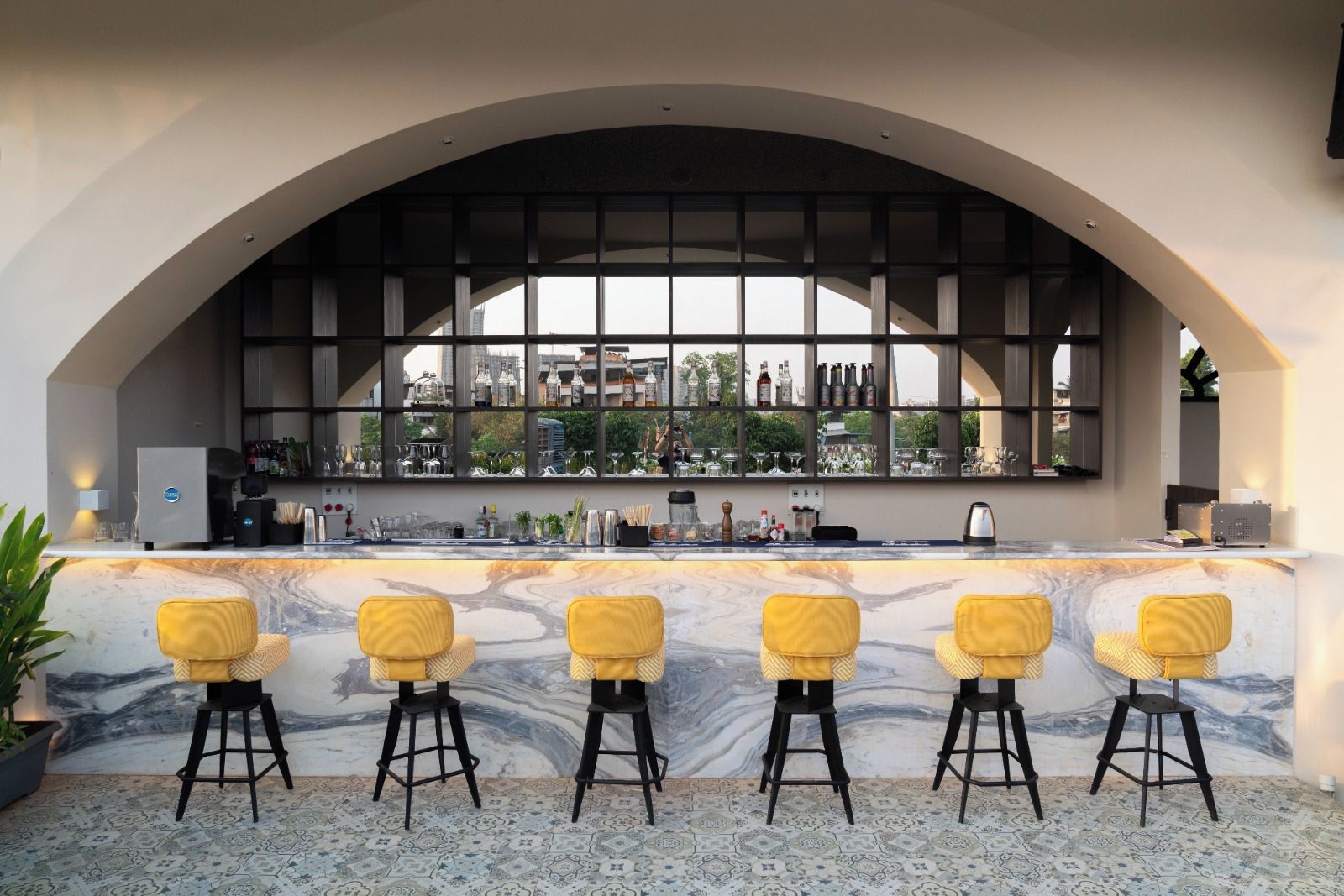 A bar area with a marble countertop, yellow bar stools, and a view of the city through large windows.