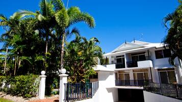 A two-story house with a white exterior, a balcony on the second floor, and a driveway leading to the entrance.