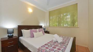 A neatly made bed with a patterned bedspread, a bedside table with a lamp, and a window with blinds.