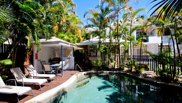A pool area with lounge chairs, a small covered seating area, and surrounding palm trees. - Seascape Holidays - Tropic Sands (Port Douglas)