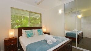 A bedroom with a bed, nightstands, a mirror, and a ceiling fan. - Seascape Holidays - Tropic Sands (Port Douglas)