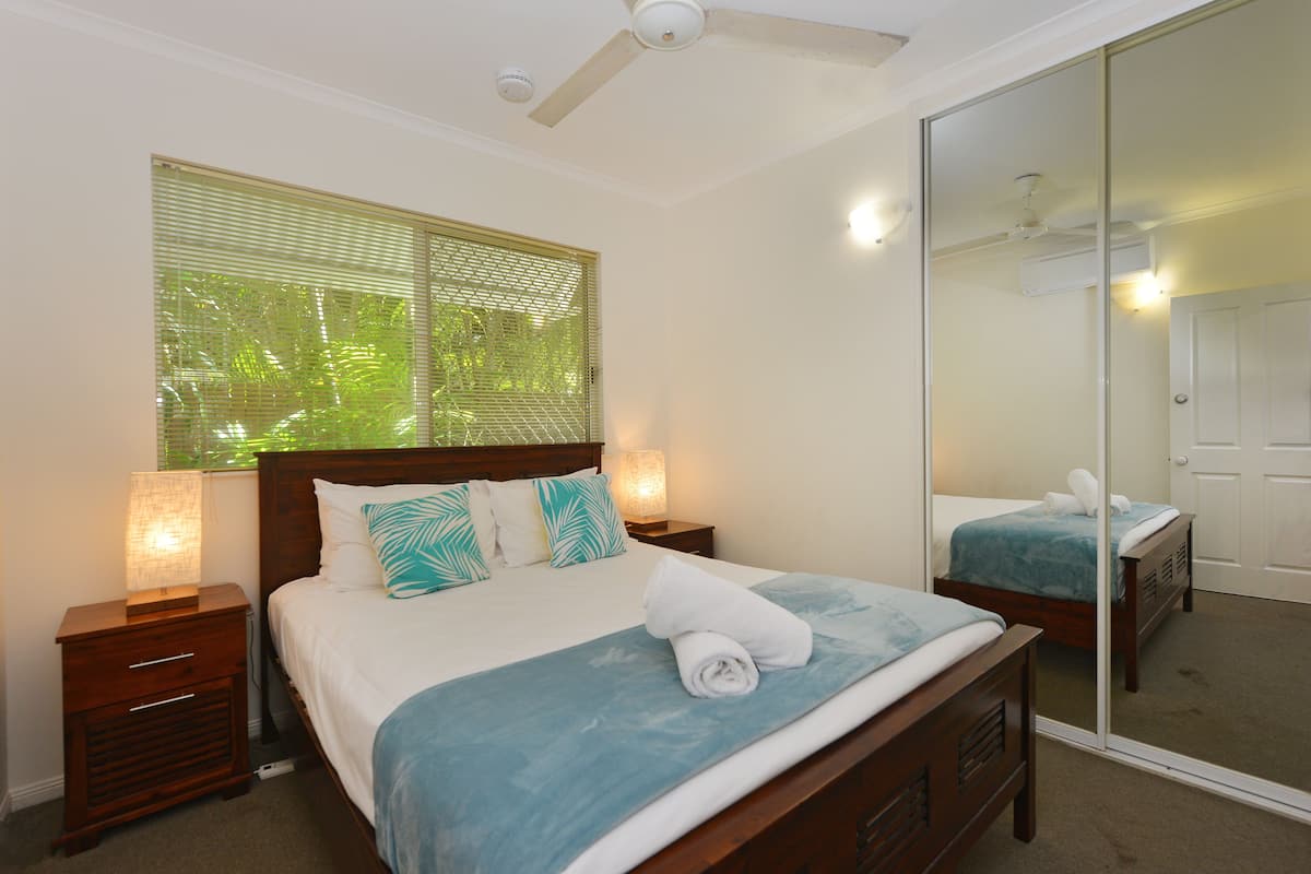 Une chambre à coucher comprenant un lit, des tables de chevet, un miroir et un ventilateur de plafond.