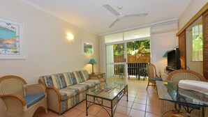 A living room with a sofa, chairs, a glass coffee table, a ceiling fan, and a TV. - Seascape Holidays - Tropic Sands (Port Douglas)