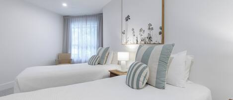 A hotel room with two beds, a nightstand, a lamp, a chair, and a large framed picture on the wall.
