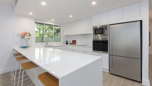 Una cocina moderna con armarios blancos, electrodomésticos de acero inoxidable y una isla central con taburetes de bar.