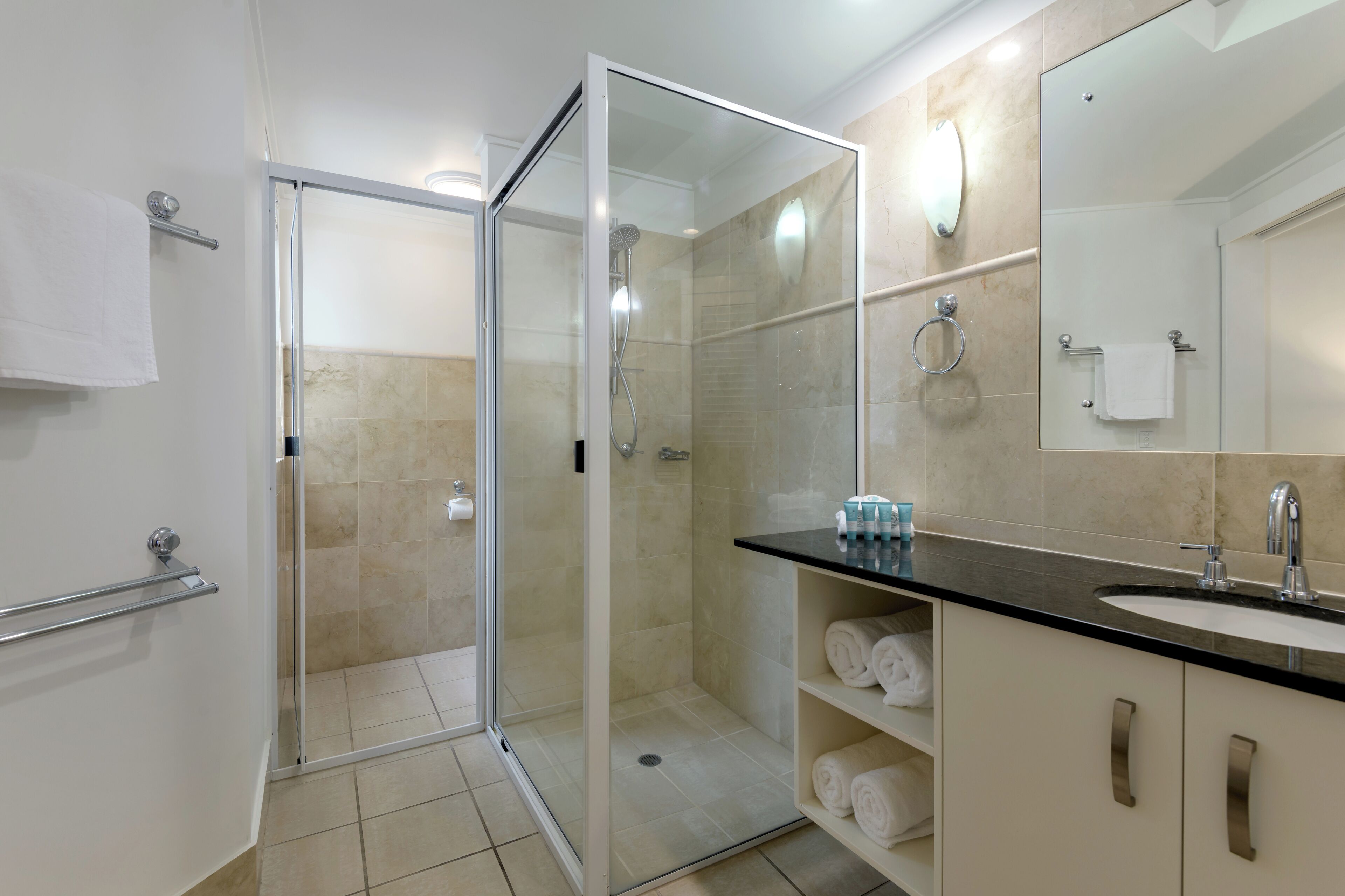 A modern bathroom with a glass-enclosed shower, a sink with a mirror, and neatly arranged towels.