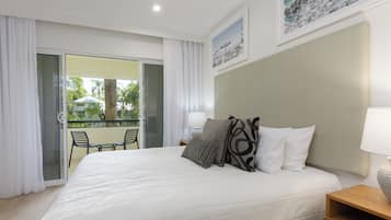 A hotel room with a large bed, a balcony with chairs, and a view of greenery.