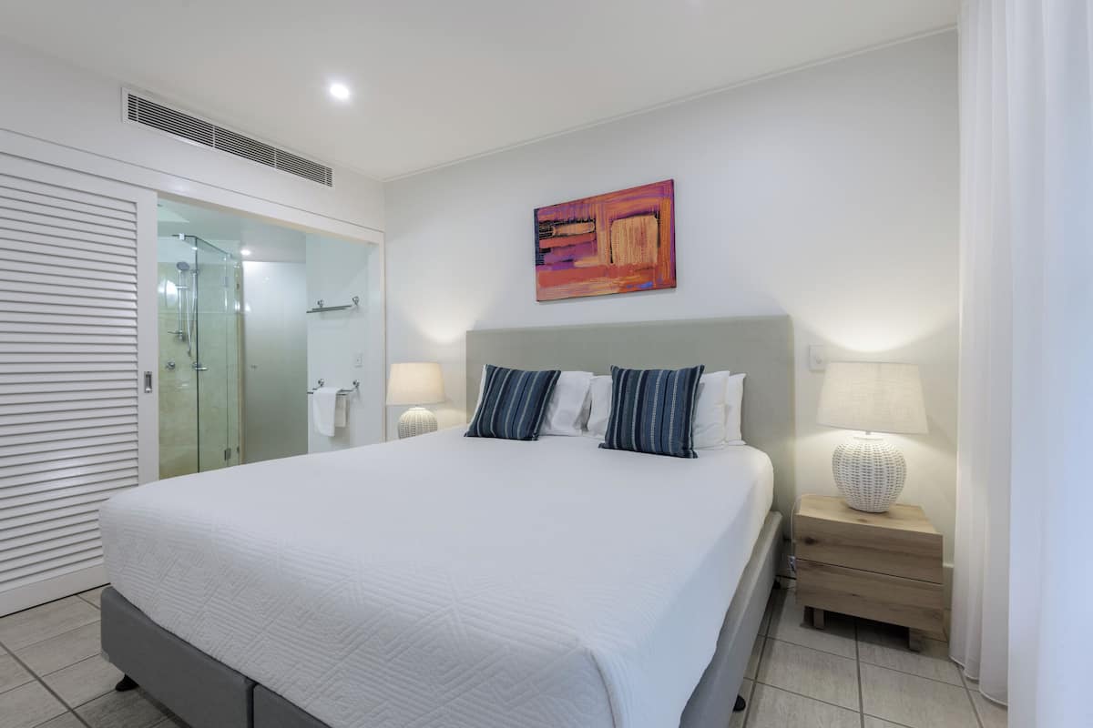 Una habitación de hotel moderna con una cama grande, una cabina de ducha de vidrio y un cuadro en la pared.