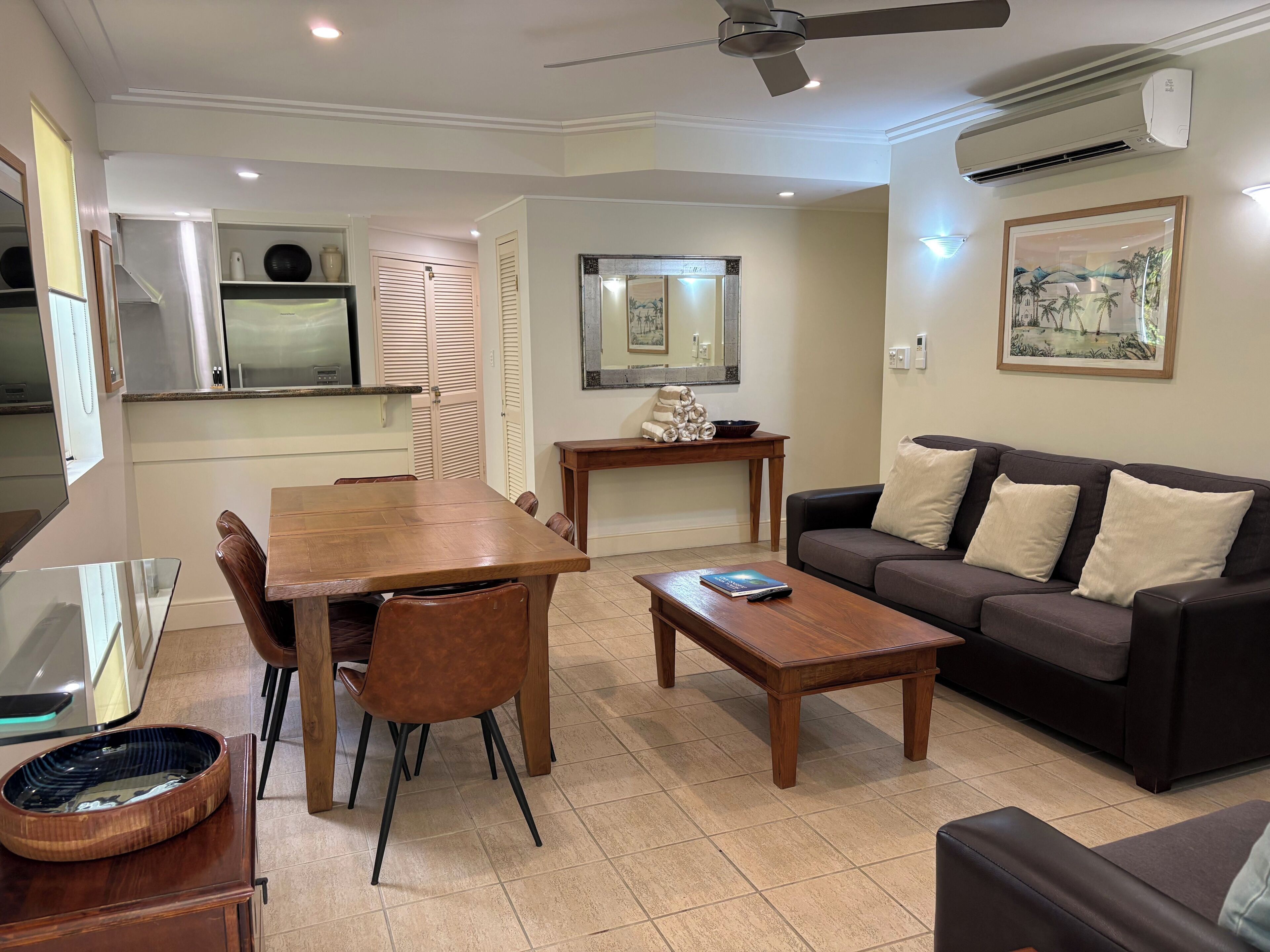 Un salon comprenant un canapé, une table basse et une table à manger. Un climatiseur est fixé au mur et un ventilateur de plafond est installé au plafond.