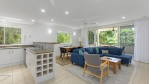 Una sala de estar moderna con un sofá azul, una mesa de comedor y una cocina con armarios blancos y una encimera.