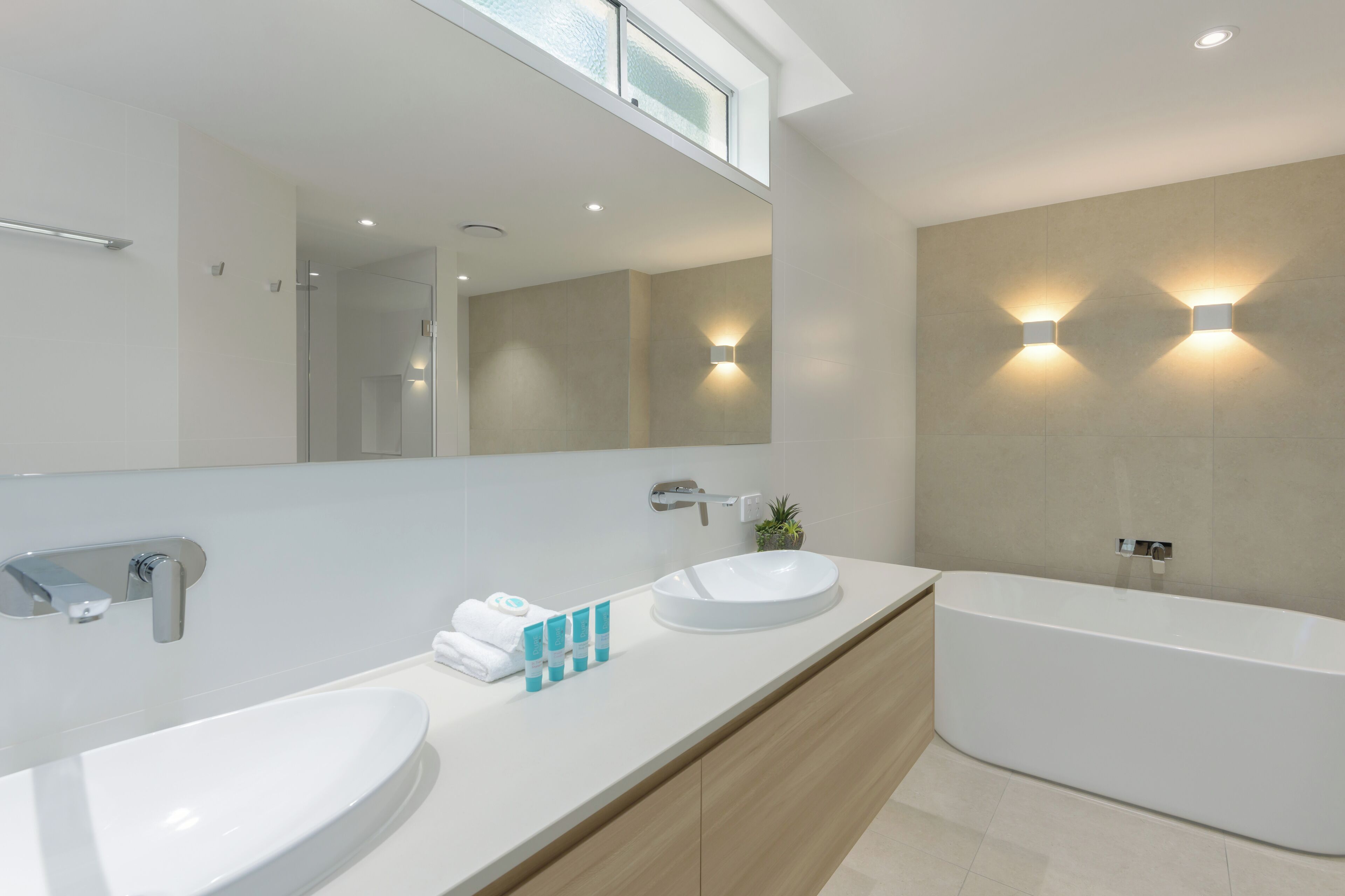 A modern bathroom with two sinks, a large mirror, and a bathtub.