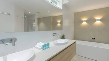A modern bathroom with two sinks, a large mirror, and a bathtub.