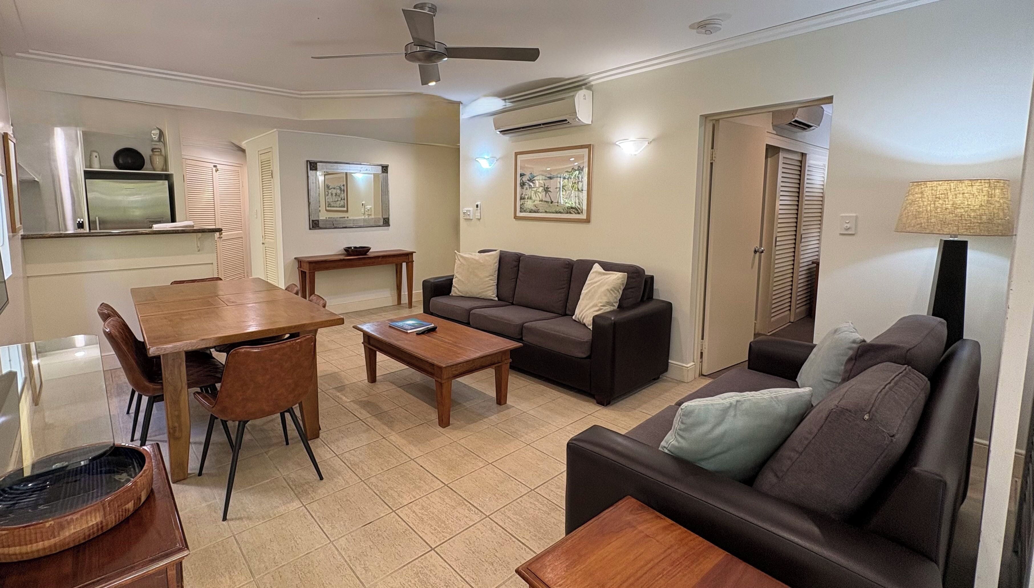 A living room with a dining area, a sofa, a coffee table, and a ceiling fan.