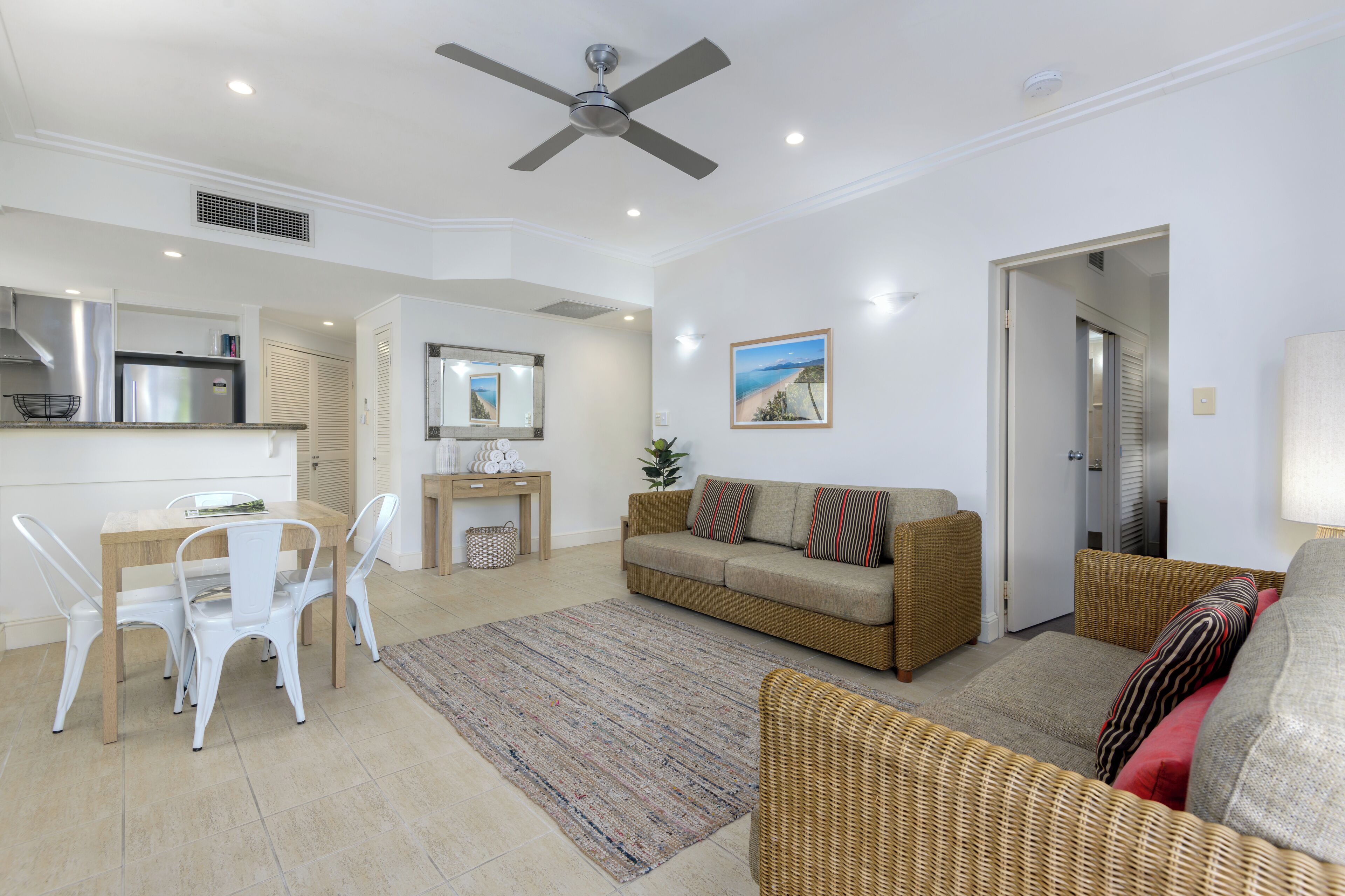 A modern living room with a dining area, a sofa, a ceiling fan, a kitchen with a refrigerator, and a painting on the wall.