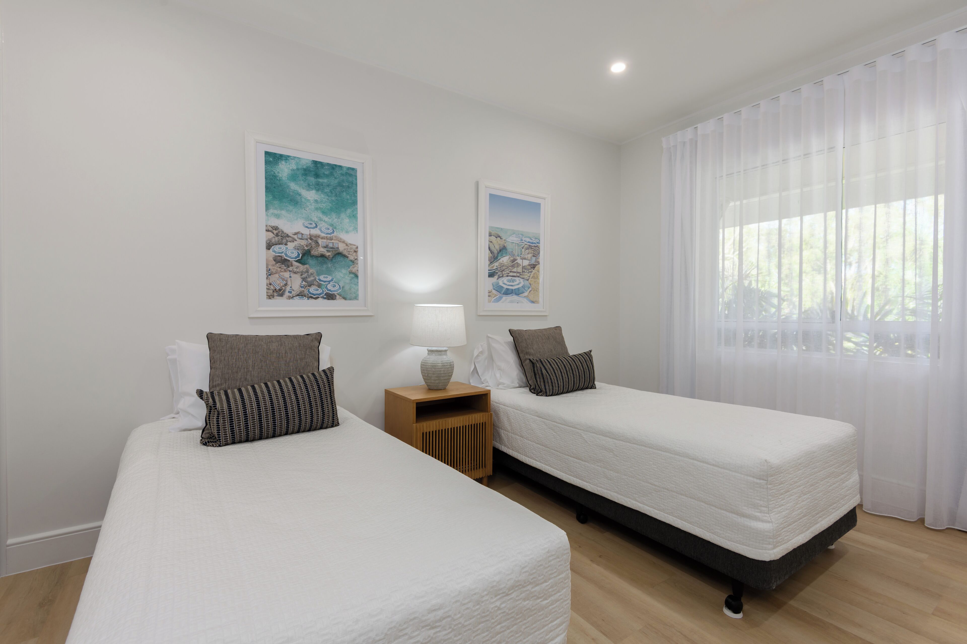 A hotel room with two beds, a nightstand with a lamp, and two framed pictures on the wall.