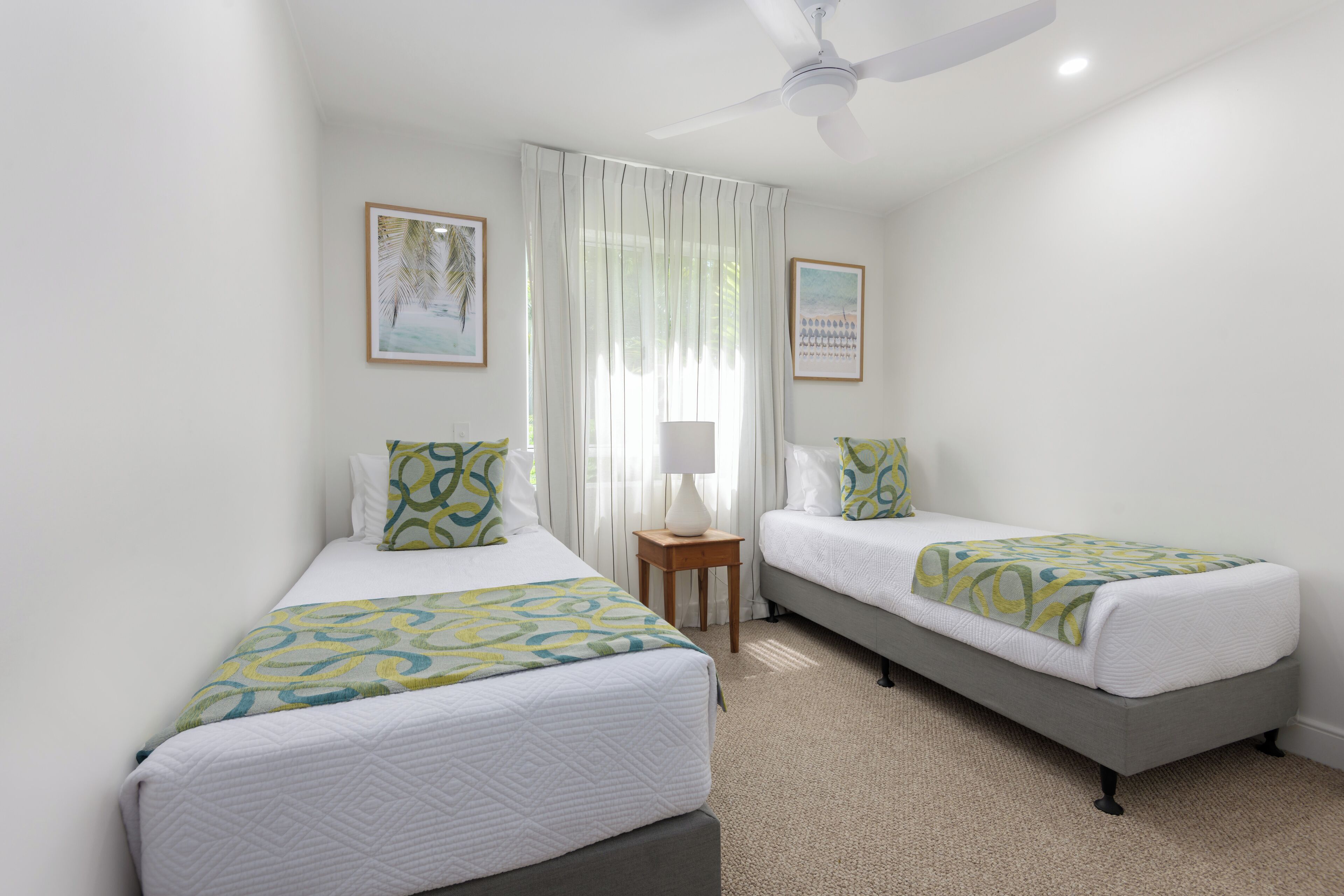 A hotel room with two beds, a ceiling fan, and a window with sheer curtains.